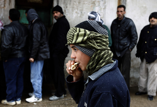BOY EAST BREAD AS OTHERS WAIT OUTSIDE BAKERY IN WESTERN SYRIA