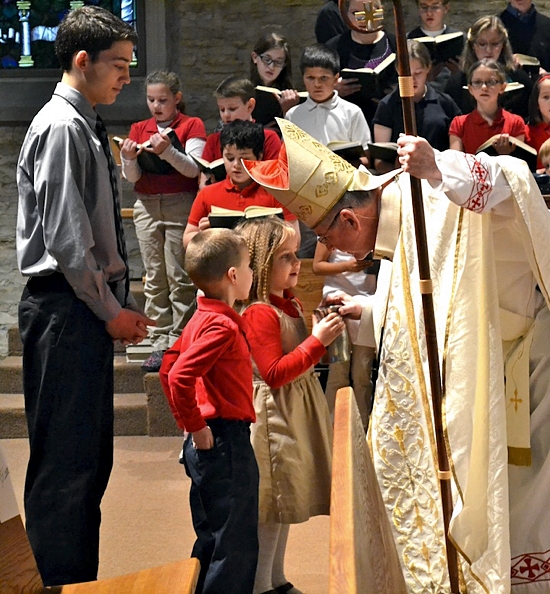 Archbishop John Nienstedt greets kindergarteners Anna Tobin and Noah Casper as they bring him the gifts during a Catholic Schools Week Mass Jan. 30 at Divine Mercy in Faribault. Mitchell Malecha, a junior at Bethlehem Academy, looks on. Photo courtesy of St. Croix Catholic School