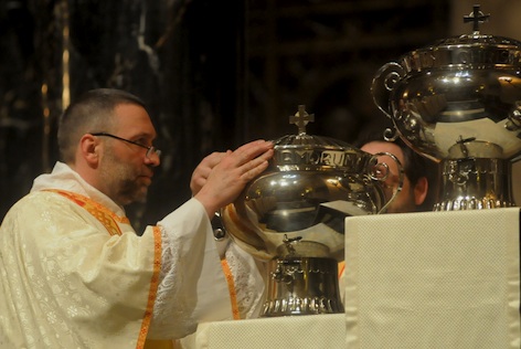 Deacon Paul Tschann places a vessel of oil on a pedestal during the Mass. Deacon Tom Michaud Jr. is behind the oils.
