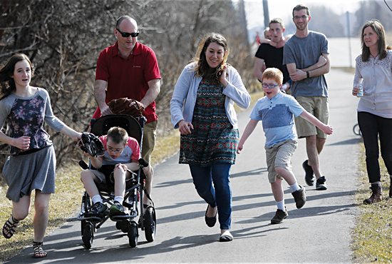 From left front, Maggie Thibault runs to a local park with Stas (in stroller), Dan, personal care attendant Brittany Wiitala and Ricky. Back left: Chuck Thibault (holding Susha), Bobby and Gretchen.