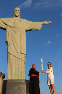 Cardinal Orani Tempesta of Rio de Janeiro and former Brazilian volleyball player Isabel Barroso hold the Olympic torch in front of the Christ the Redeemer statue in Rio de Janeiro Aug. 5. CNS photo/Lise Alves