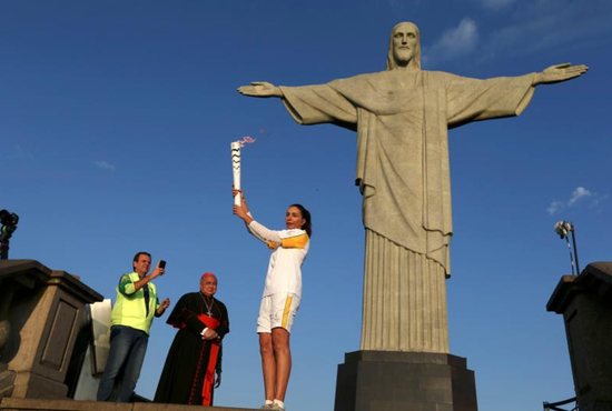 Former Brazilian volleyball player Isabel Barroso holds the Olympic torch Aug. 5 next to the Christ the Redeemer statue as Rio de Janeiro Mayor Eduardo Paes and Cardinal Orani Tempesta look on. CNS photo/Pilar Olivares, Reuters