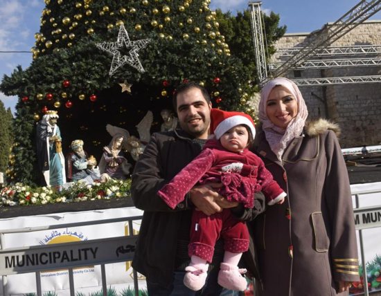 Muslim Palestinian Ashraf Natsheh, 28, holds his daughter Lara, 10 months, next to his wife, Shahad, 26, in front of the Christmas tree in Manger Square Dec. 5 in Bethlehem, West Bank. They had been unable to get into Bethlehem last year. CNS photo/Debbie Hill