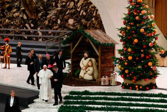 Pope Francis is assisted by his aide, Sandro Mariotti, as he walks down stairs during his general audience in Paul VI hall at the Vatican Dec. 7. The Nativity scene and Christmas tree decorations are from the Mexican state of Queretaro. CNS photo/Paul Haring