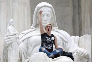 A protester sits on the lap of "Lady Justice" on the steps of the U.S. Supreme Court building in Washington as demonstrators storm the steps and doors of the building Oct. 6 while Judge Brett Kavanaugh, a Catholic, is sworn in as an associate justice inside.