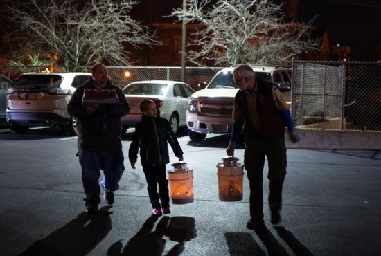 Aaron Emery, left, and his son, Andrew Emery of Lafayette, Ind., help Brian Duane carry the Peace Light, contained in specially-equipped buckets, into the Cathedral of St. Mary of the Immaculate Conception Dec. 4. The flame is originally kindled from the place in Bethlehem, West Bank, where Christ was born, flown to Europe and the United States, then distributed by volunteers like Duane across the country.