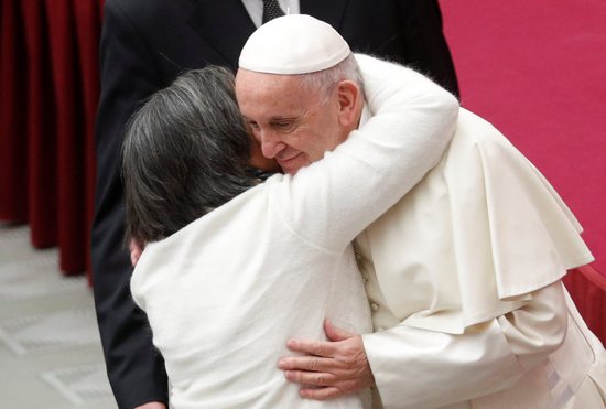 A woman embraces Pope Francis as he arrives to lead his general audience in Paul VI Hall Dec. 12 at the Vatican.