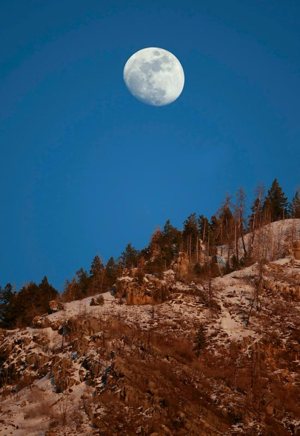As the evening sun sets on Y Mountain, the moon rises above the tree line near Provo, Utah. The congressionally mandated Fourth National Climate Assessment, released Nov. 23 by the White House, projects that climate change will cost the country hundreds of billions of dollars a year by 2090.