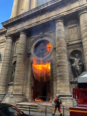 A firefighter is seen as flames shoot through the front door of St. Sulpice Church in Paris March 17, 2019, in this still image taken from social media. Vandals and arsonists have targeted French churches in a wave of attacks that has lasted nearly two months.