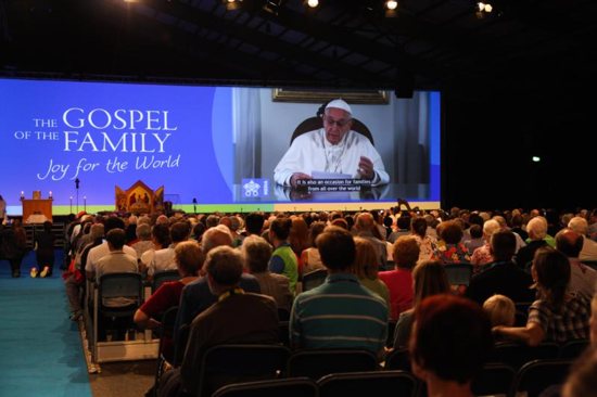 Attendees watch Pope Francis on a screen during the opening ceremony of the World Meeting of Families in Dublin Aug. 21, 2018. The Vatican announced the theme Pope Francis has chosen for the next World Meeting of Families, which will be in Rome June 23-27, 2021: "Family love: a vocation and a path to holiness." 