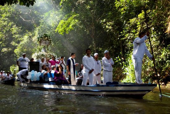 A priest in a boat holds a Bible as he leads pilgrims in prayer along during an annual river procession and pilgrimage on the Caraparu River in Santa Izabel