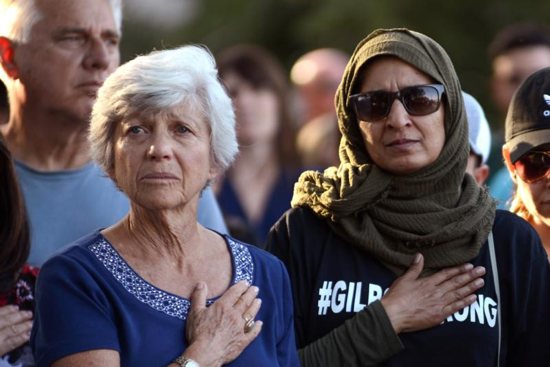 Women attend a candlelight vigil outside Gilroy City Hall in California July 29, 2019, during the singing of the National Anthem honoring those who died and were injured during a mass shooting at the Gilroy Garlic Festival. The Diocese of San Jose held a bilingual prayer vigil July 29 for victims, survivors and first responders at St. Mary Church in Gilroy in response to the the shooting a day earlier that claimed three lives and injured 12 others.