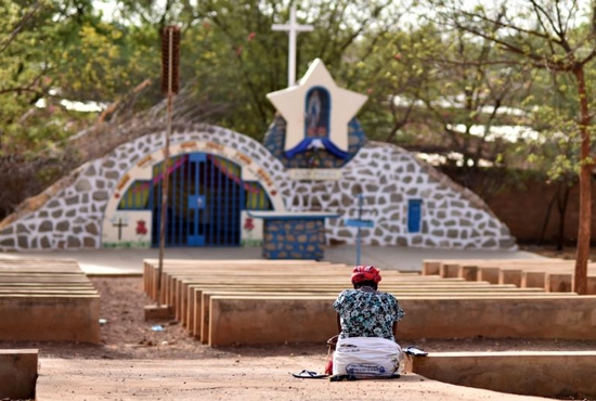 A displaced Christian woman prays in front of a grotto with a statue of Mary in Kaya, Burkina Faso
