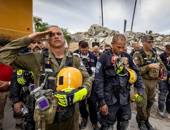 A member of the Israeli search and rescue team salutes in front of the rubble that once was Champlain Towers South during a prayer ceremony and a moment of silence in Surfside, Fla., July 7, 2021. 