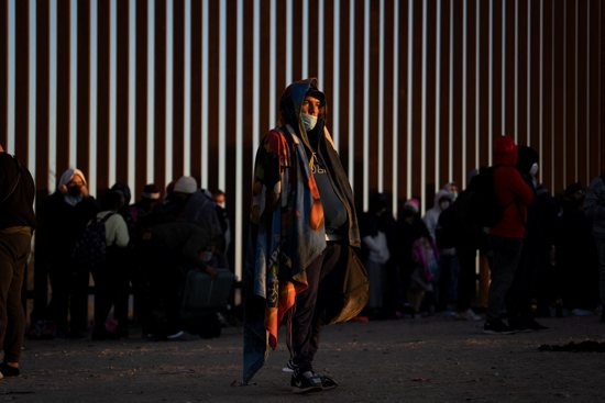 Migrants seeking asylum in Yuma, Ariz., Jan. 23, 2022, stand near the border fence while waiting to be processed by the U.S. Border Patrol. 