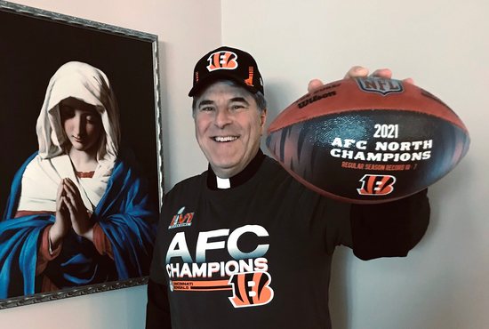 Father Tom Wray, Catholic chaplain of the Cincinnati Bengals, poses for a photo with the 2021 AFC North Champions ball Feb. 8, 2022. As part of his chaplaincy, Father Wray has conversations and provides spiritual guidance to those who work for the Bengals franchise. 