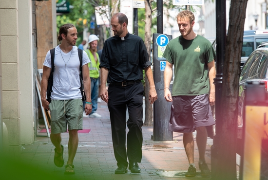 Colin Miller, from left, Father James Boric, rector of the Basilica of the National Shrine of the Assumption of the Blessed Virgin Mary, and Nathan Belk walk along Charles Street Aug. 19, 2019, as part of their urban ministry outreach in Baltimore.